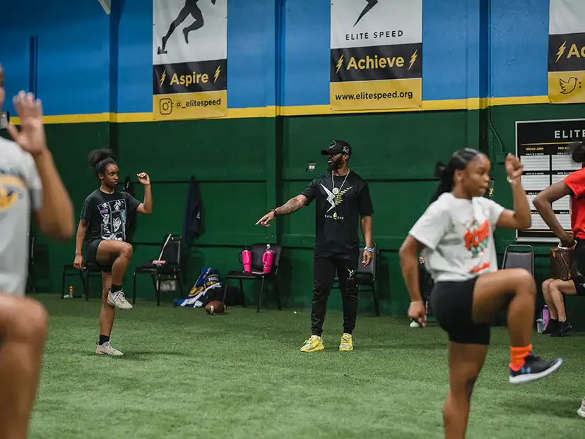 Girls running a knee-drive warm-up with an Elite Speed coach on the indoor turf in Granite City, Illinois