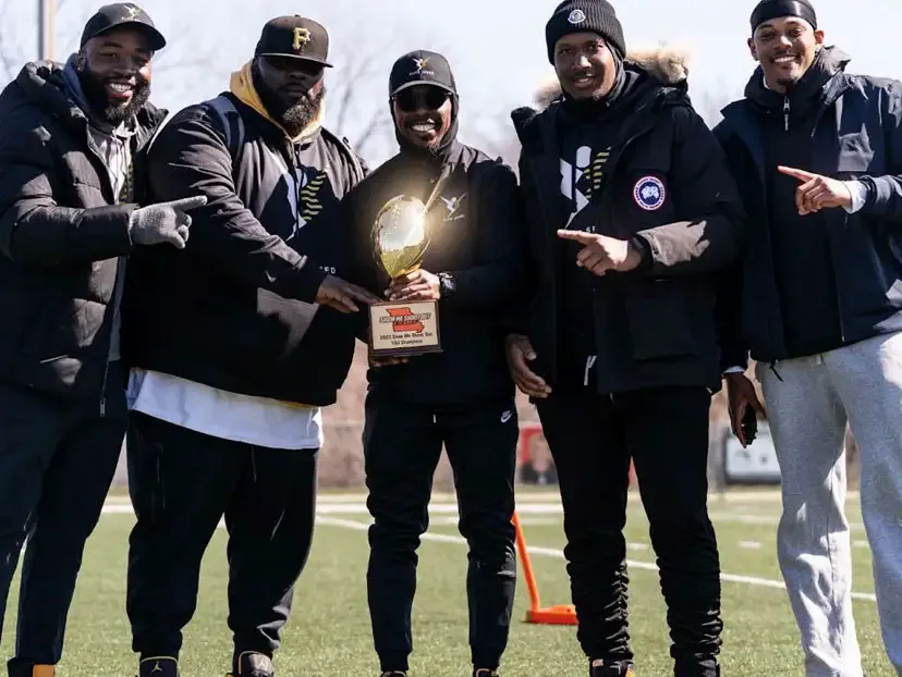 Five Elite Speed coaches on a football field holding a championship trophy